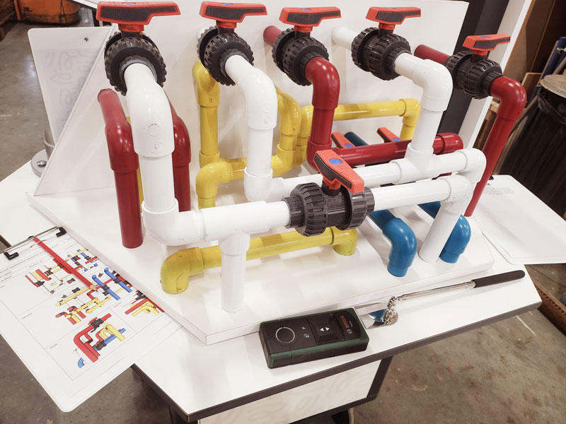 Maquette de tuyauterie et de vannes colorées utilisée dans l’exposition « Au cœur de la maintenance » pour illustrer les métiers de la maintenance industrielle.