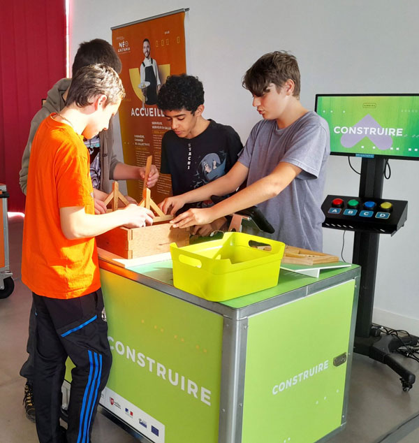 Des adolescents participent à un atelier pratique du pôle "Construire" dans l’exposition "Destination Planète NéoAkitania" de Cap Métiers Nouvelle-Aquitaine, découvrant les métiers liés au bâtiment et aux travaux publics.
